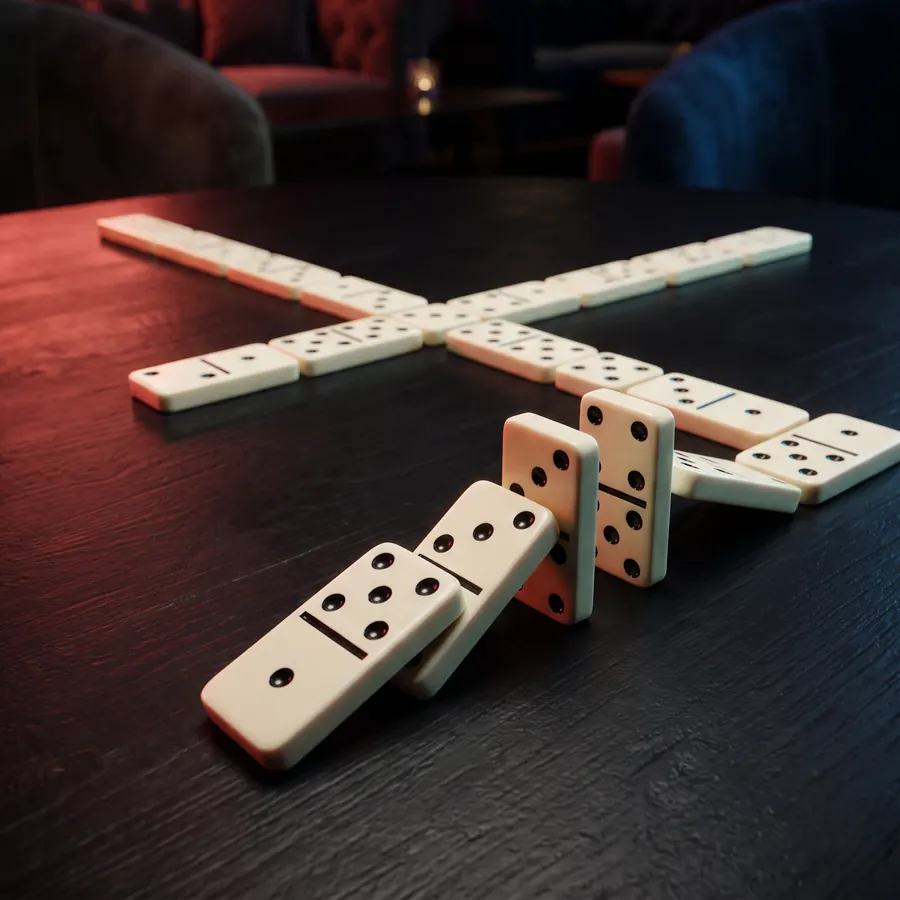 Cream domino tiles laid out in a branching chain across a dark table, a few standing on edge in the foreground.