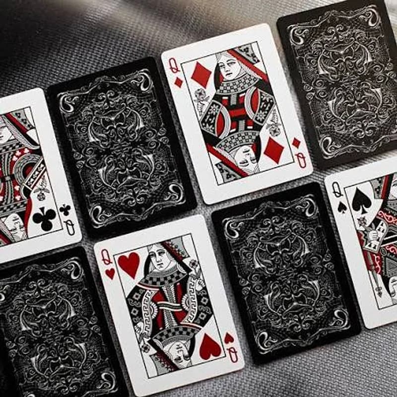 Black-backed playing cards spread face up and face down on a dark cloth: the queens of diamonds, hearts, clubs and spades in red and black.