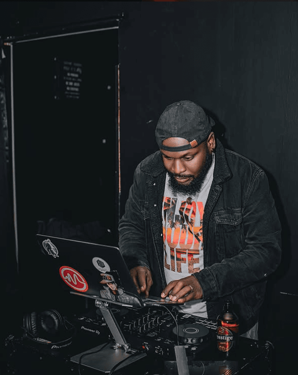 Saan behind a Pioneer DJ controller in a dark room, hands on the deck.